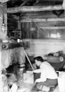Bert Gallistel crouching at shack fireplace