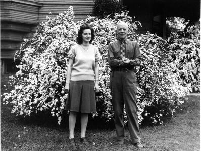 With secretary Alice Harper, 1938, in front of flowering shrub