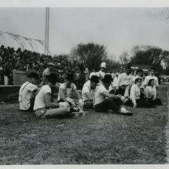 Phi Omega Beta pledges sitting on the sidelines of a football game, next to the Stout Cheerleaders