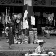 Shop featuring pails, kettles, umbrellas, shirts; Lao woman with food stall on street in front of shops