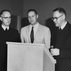 Three unidentified men standing by lectern.