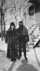 Two people bundled up in front of farmhouse