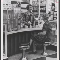 A clerk helps a woman seated at the cosmetics counter