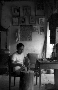 Chinese craftsman in shop, family photos on wall, pounding metal on anvil
