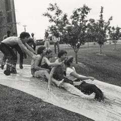 Student playing on plastic water slide on university grounds