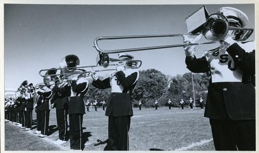 Stout marching band performing on the football field, trombone section up close