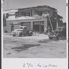 Two men stand outside of a wrecked drugstore