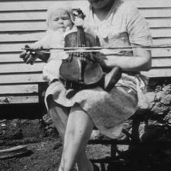Baby holds violin on woman's lap