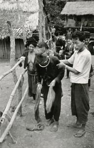 An elderly Blue Hmong (Hmong Njua) man is being helped along a path in a Hmong village in the vicinity of Muang Vang Vieng in Vientiane Province