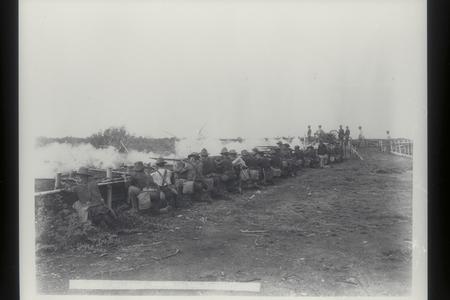 U.S. soldiers fire rifles in volleys from behind a barricade, San Roque, 1899