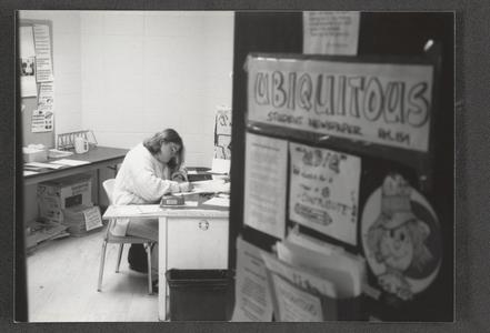 Student writing at desk in Ubiquitous (student newspaper) office