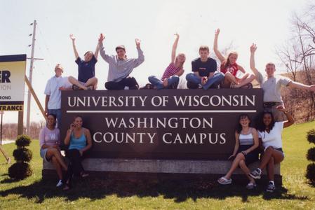 Students sitting around campus main entrance sign along University Drive