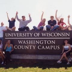 Students sitting around campus main entrance sign along University Drive