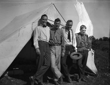 Four men standing outside tent
