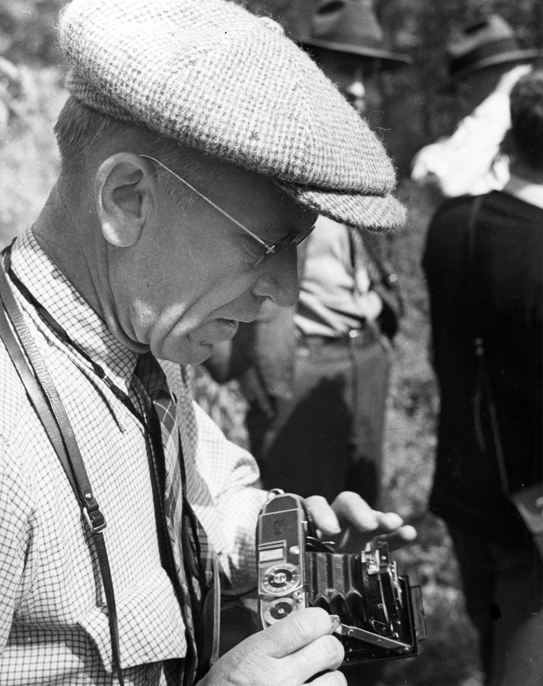 With camera, wearing tweed cap and looking down, 1935