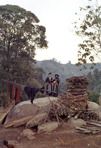 Two White Hmong women and infant stand near a pile of firewood in Houa Khong Province
