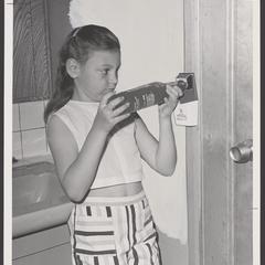 A young girl tries out a bottle opener on a bottle of soda pop