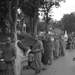 Morning, laity providing rice and food for local monks which is placed inside their food containers carried in bags with shoulder straps, laymen standing and offering food