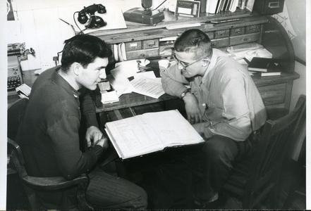 Stout Student Association members Charlie and Lewie sitting at desk looking at a ledger book