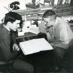 Stout Student Association members Charlie and Lewie sitting at desk looking at a ledger book
