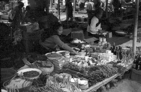 Woman selling soap powder, soap, condensed milk, bottles of sauce, dried foods at stand