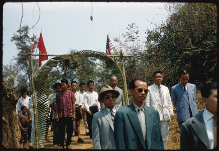 Inauguration of United States Operations Mission (USOM) dam--officials arriving under palm framed archway with Lao and United States flags