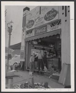 Two men stand in the wreckage of a drugstore's front window