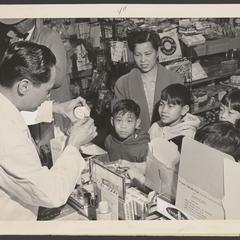 A pharmacist offers a liquid vitamin sample to customers