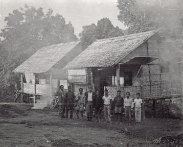Nine village men stand in front of two houses in Houei Kong Cluster in Attapu Province
