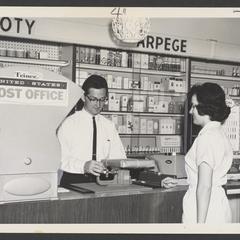 Man weighs a package for a woman at a drugstore post office substation