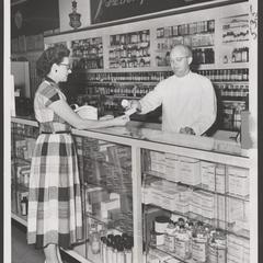 A pharmacist serves a customer at the prescription counter