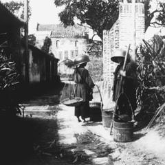 [Two women carrying materials]