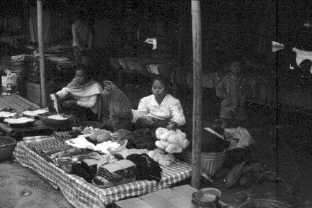 Lao woman in foreground selling cloth skirt borders and skeins of silk, woman with noodles in background