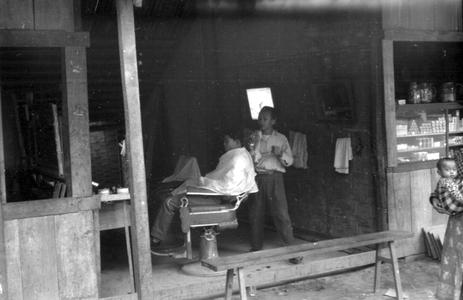 Barber shop and customer, baby in carrying cloth on right, business district
