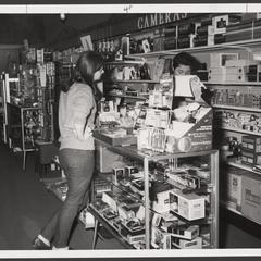 A woman stands at a camera counter in a drugstore
