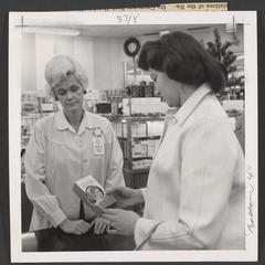 Two women stand at a drugstore counter looking at a box of hair dye