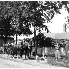 Kate and Ellen Nelson in front of their house with dog and horse-drawn carriage
