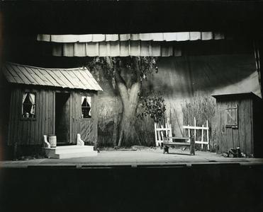 Stage set for an outdoor scene, a run-down one-room house, stable, and yard