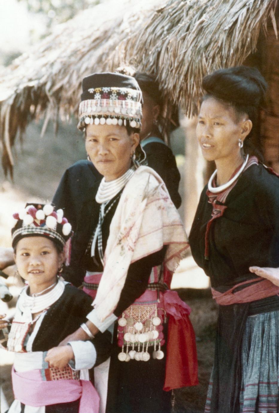 Two Hmong women and girl stand near a house in Houa Khong Province