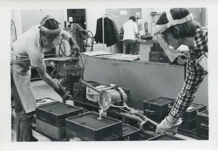 Two male students pouring molten metal into a mold
