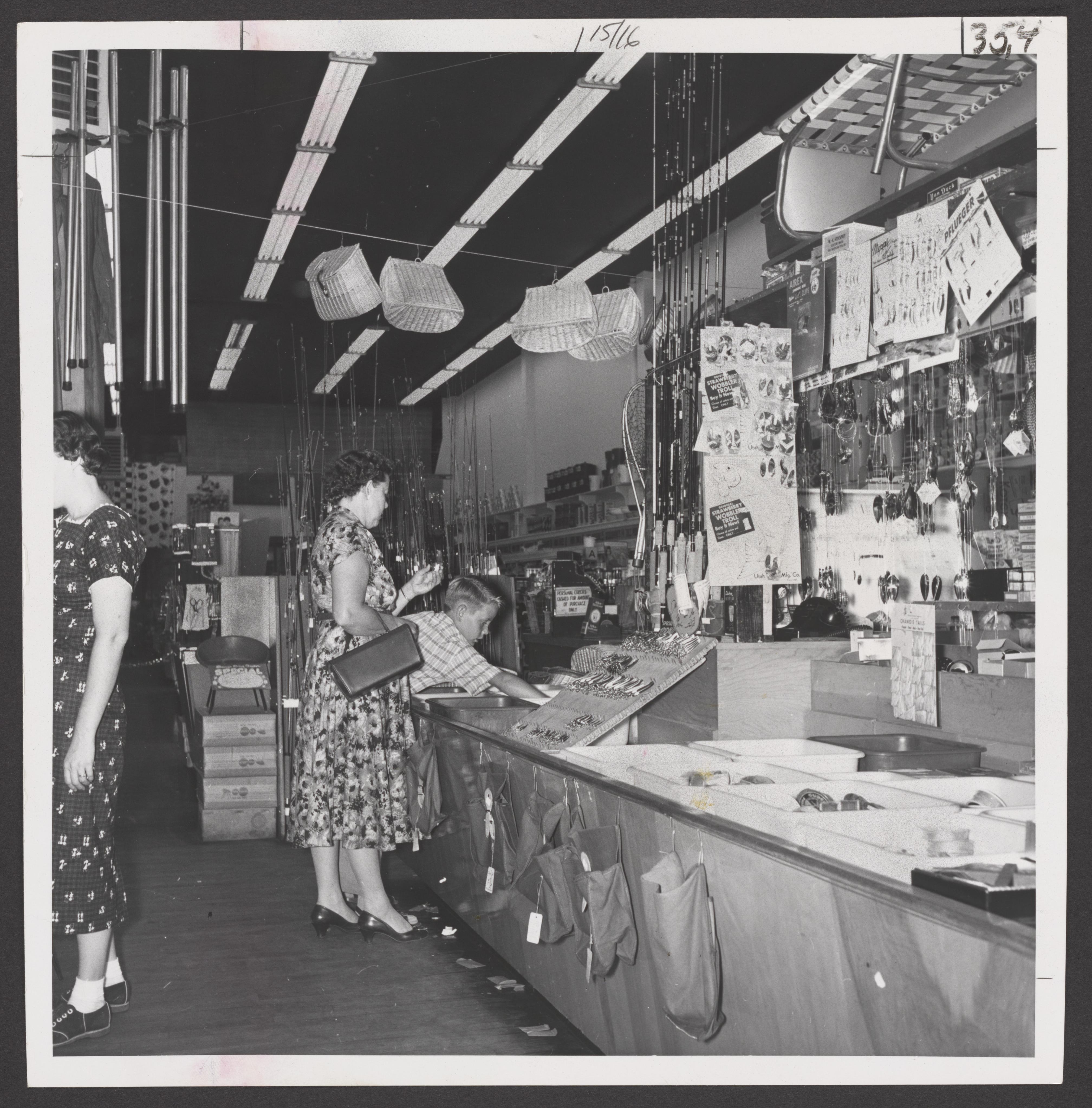 A woman and young boy look at fishing gear in a drugstore display - UWDC -  UW-Madison Libraries