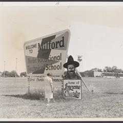 A woman stands next to two large road signs in a field