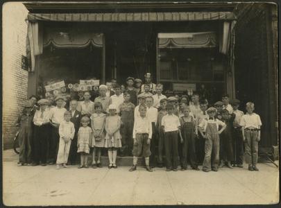 Group of young children standing on steps outside of a shop.