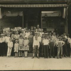 Group of young children standing on steps outside of a shop.