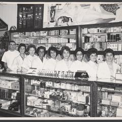 Pharmacist and cosmetics clerks stand in a row behind counter