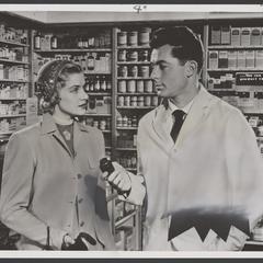 Male drugstore employee hands a jar to a woman