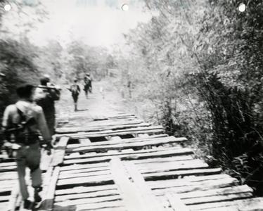Soldiers on patrol cross primitive bridge on Route 11 between Attapu and Saravan