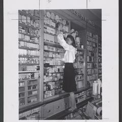 Woman stands on built-in ledge to reach higher shelves in a drugstore