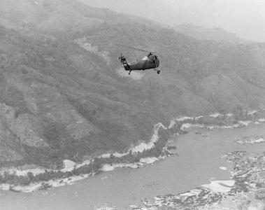 A H-34 helicopter flies over the mountains and Mekong River in Houa Khong Province