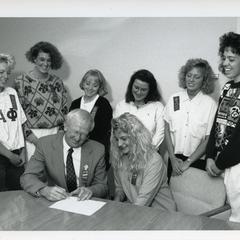 Chancellor Charles Sorensen signing a document while Alpha Phi members look on